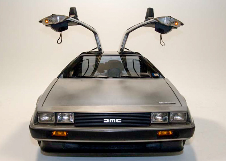A DeLorean DMC-12 with both gullwing doors raised, showing the stainless-steel body