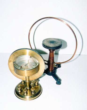 A brass tangent galvanometer with a large vertical wire coil surrounding a compass needle on a graduated dial