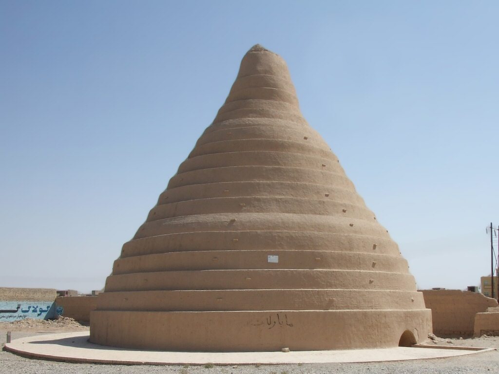 A tall conical adobe yakhchāl dome standing in the desert in Yazd province, Iran