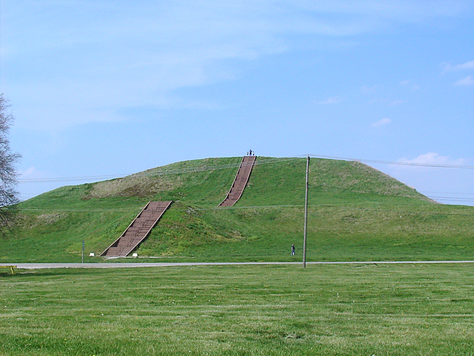 Monks Mound at Cahokia, a broad flat-topped earthen pyramid rising in terraces above green grass under a summer sky