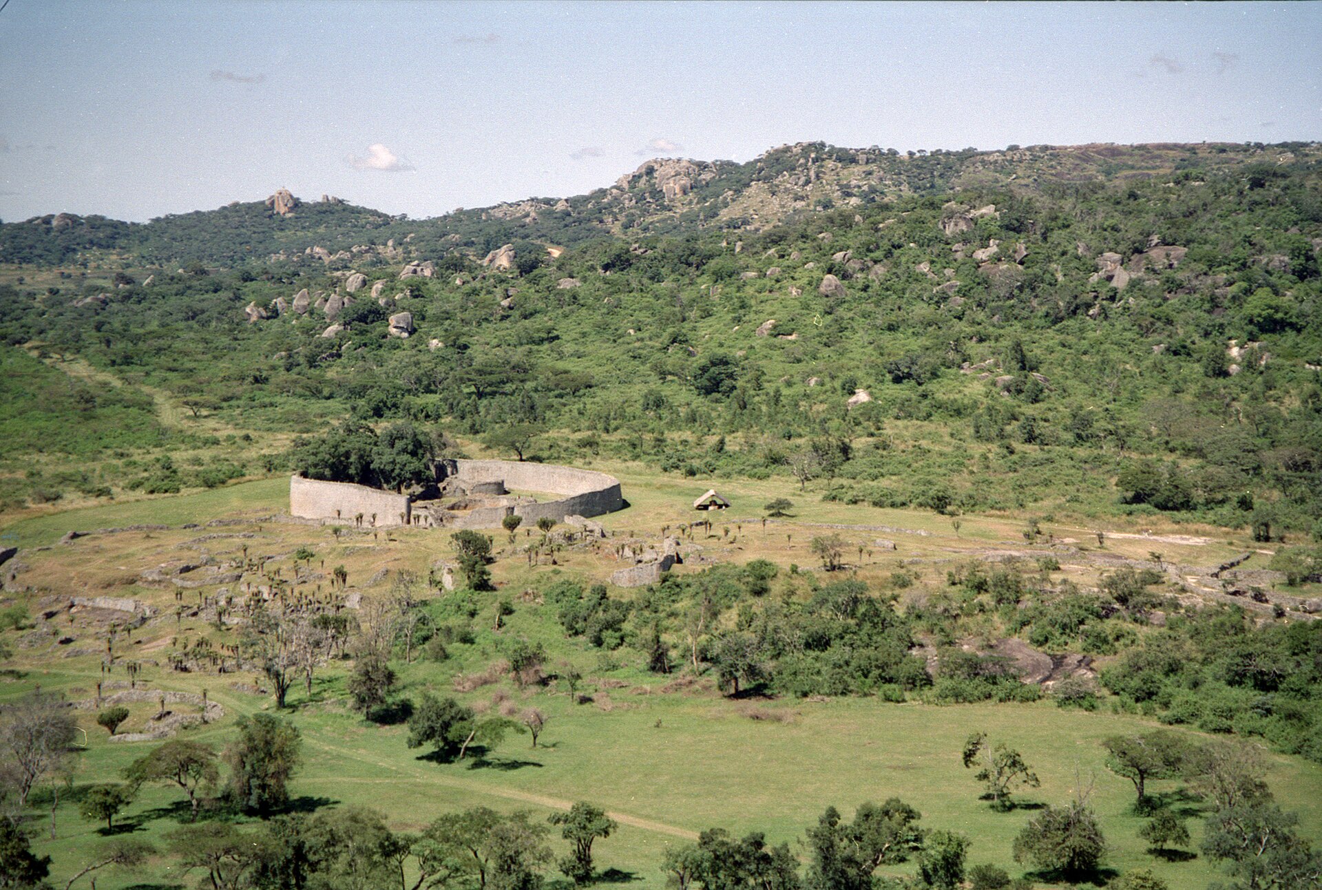 The dry-stone granite wall of the Great Enclosure at Great Zimbabwe, curving across the hillside with the valley ruins below